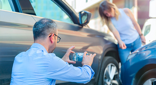 Father and daughter taking photos os damage to their car with a smart phone
